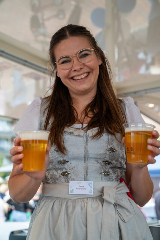Fröhliche Mitarbeiterin auf dem "WiesnZauber", die dabei ist zwei Becher Bier auszugeben.